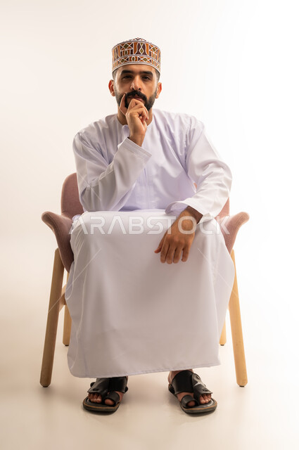 اتخاذ القرارات وحل المشكلات ،التفكير و شرود الذهن , النظر بتمعن والتخطيط للمستقبل, محاولة إيجاد الحلول , بورتريه لشاب عربي خليجي عماني يرتدي الدشداشة والكمة ينظر الى الكاميرا, خلفية بيضاء .