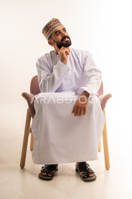 Looking carefully and planning for the future, thinking and trying to find a solution to problems, absent-mindedness and making decisions with focus, portrait of a young Arab Gulf Omani man wearing a dishdasha and a kummah looking at something, white background.