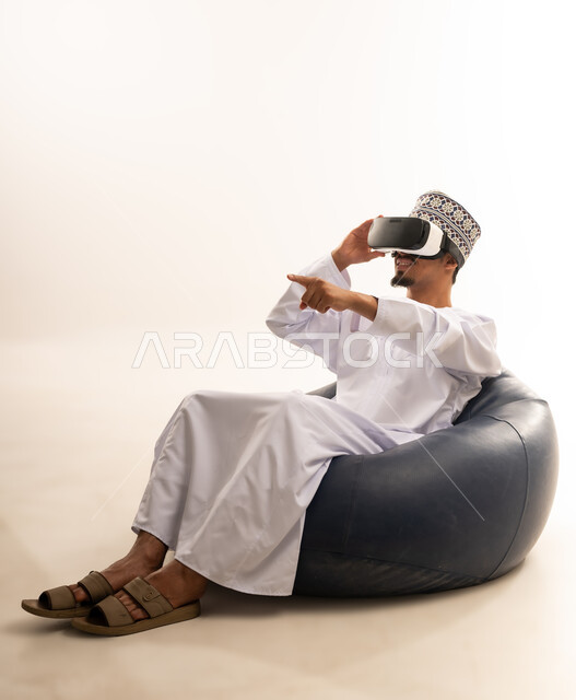 Integration and interaction with the imaginary world, use of advanced techniques and technology, portrait of a young Arab Gulf Omani man wearing a dishdasha and an Omani kummah, wearing VR glasses, watching virtual reality movies, spending leisure time in an enjoyable way, white background