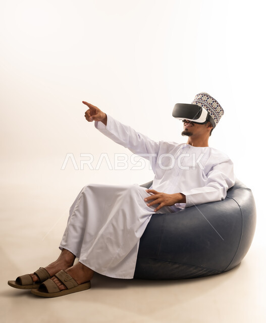 الاندماج والتفاعل مع العالم الخيالي، استخدام التقنيات والتكنولوجيا المتطورة، بورتريه  لشاب عربي خليجي عماني يرتدي الدشداشة والكمه العمانية يضع نظارة في آر على عينيه، مشاهدة أفلام الواقع الافتراضي، قضاء أوقات الفراغ بشكل ممتع، خلفية بيضاء