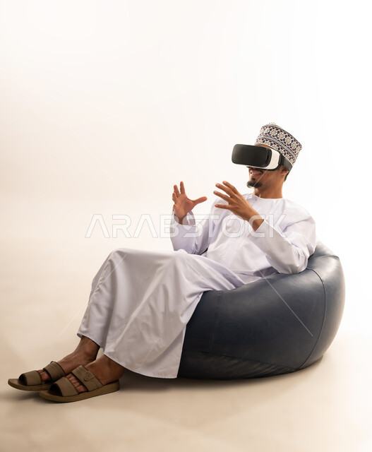 الاندماج والتفاعل مع العالم الخيالي، استخدام التقنيات والتكنولوجيا المتطورة، بورتريه  لشاب عربي خليجي عماني يرتدي الدشداشة والكمه العمانية يضع نظارة في آر على عينيه، مشاهدة أفلام الواقع الافتراضي، قضاء أوقات الفراغ بشكل ممتع، خلفية بيضاء