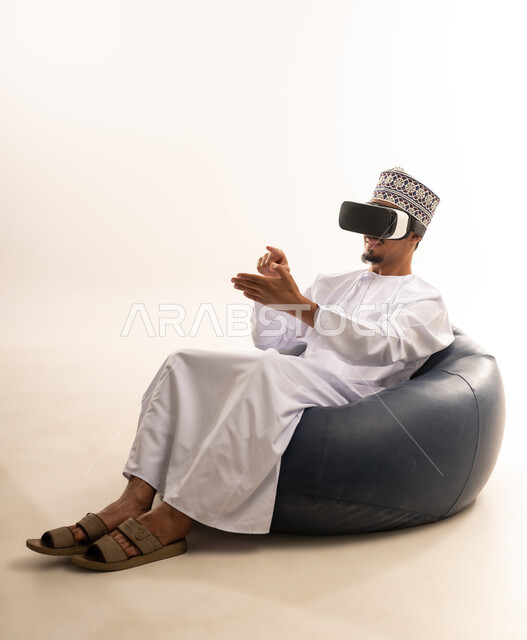 Integration and interaction with the imaginary world, use of advanced techniques and technology, portrait of a young Arab Gulf Omani man wearing a dishdasha and an Omani kummah, wearing VR glasses, watching virtual reality movies, spending leisure time in an enjoyable way, white background