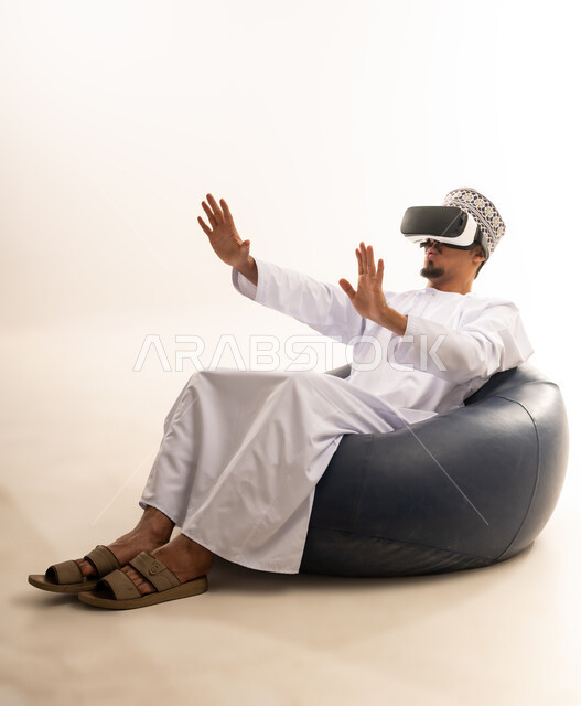 Integration and interaction with the imaginary world, use of advanced techniques and technology, portrait of a young Arab Gulf Omani man wearing a dishdasha and an Omani kummah, wearing VR glasses, watching virtual reality movies, spending leisure time in an enjoyable way, white background