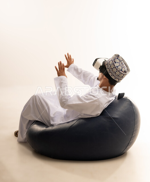 Integration and interaction with the imaginary world, use of advanced techniques and technology, portrait of a young Arab Gulf Omani man wearing a dishdasha and an Omani kummah, wearing VR glasses, watching virtual reality movies, spending leisure time in an enjoyable way, white background