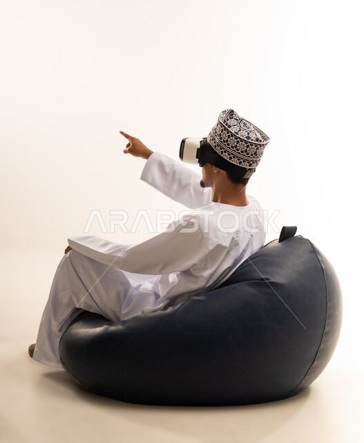 الاندماج والتفاعل مع العالم الخيالي، استخدام التقنيات والتكنولوجيا المتطورة، بورتريه  لشاب عربي خليجي عماني يرتدي الدشداشة والكمه العمانية يضع نظارة في آر على عينيه، مشاهدة أفلام الواقع الافتراضي، قضاء أوقات الفراغ بشكل ممتع، خلفية بيضاء