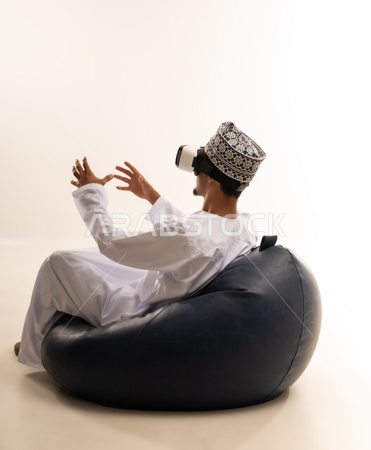 الاندماج والتفاعل مع العالم الخيالي، استخدام التقنيات والتكنولوجيا المتطورة، بورتريه  لشاب عربي خليجي عماني يرتدي الدشداشة والكمه العمانية يضع نظارة في آر على عينيه، مشاهدة أفلام الواقع الافتراضي، قضاء أوقات الفراغ بشكل ممتع، خلفية بيضاء