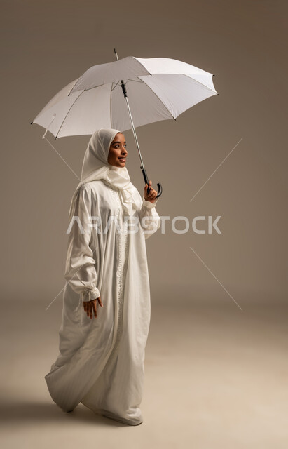 Gestures indicating happiness in performing Hajj and Umrah rituals, portrait of a young Arab Gulf Muslim woman wearing Ihram clothes holding an umbrella, Hajj season 2025, the fifth pillar of Islam, white background