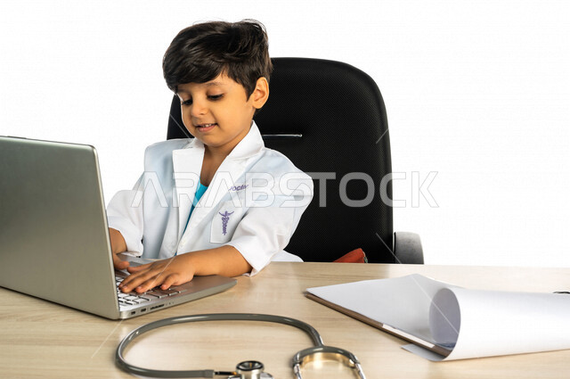 Portrait of a Saudi Arabian Gulf boy, wearing a doctor's uniform, using a laptop, a little doctor, dreaming of becoming a doctor, future profession, concept of medicine, using modern technical devices, white background, distance study, e-learning