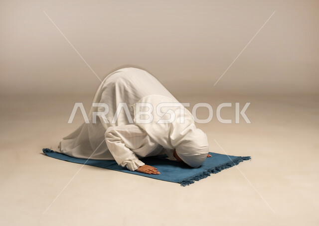 Worship and drawing closer to God, performing the second pillar of the five pillars of Islam, a portrait of a young Arab Gulf woman wearing a hijab and a white abaya performing the obligatory prayer on her own prayer rug with humility and serenity, white background