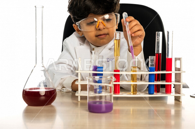Portrait of a Saudi Arabian Gulf boy, wearing a white coat, using test tubes to conduct experiments, conducting chemical experiments and reactions in the laboratory, experiments and scientific research, studies and analyzes, chemicals, future profession,