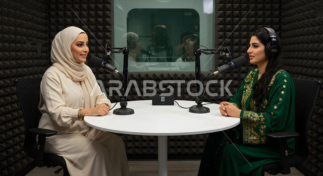 اجراء حوار اذاعي مباشر (بودكاست) عبر برامج التواصل الاجتماعي، ايماءات تدل على الحماس، استخدام التقنيات الحديثة, سيدتان عربيتان خليجيتان مبتسمتان ترديان العباءة وسماعة الرأس, مقابلة عمل داخل الاستديو, تعابير السعادة والسرور، معدات وأجهزة تسجيلات الصوت