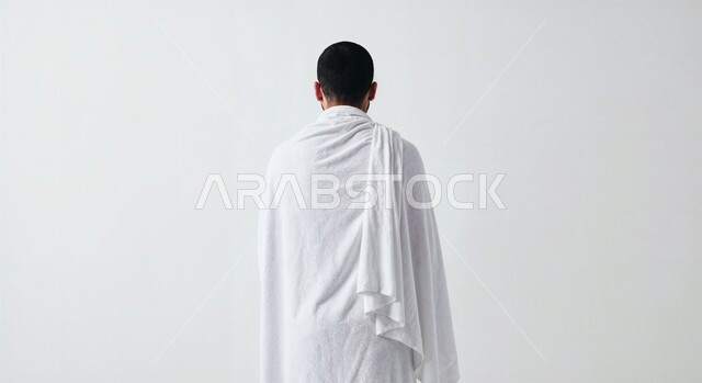Worship and closeness to God, the concept of the pillars of Islam and performing religious duties, a close-up portrait from the back of a Saudi Arabian Gulf pilgrim wearing Ihram clothes performing the Hajj and Umrah rituals, white background