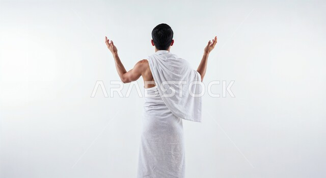 Worship and drawing closer to God, the concept of the pillars of Islam and performing religious duties, raising hands and supplicating with humility and supplication, close-up portrait from the back of a Saudi Arabian Gulf pilgrim wearing Ihram clothes performing Hajj and Umrah rituals, white background