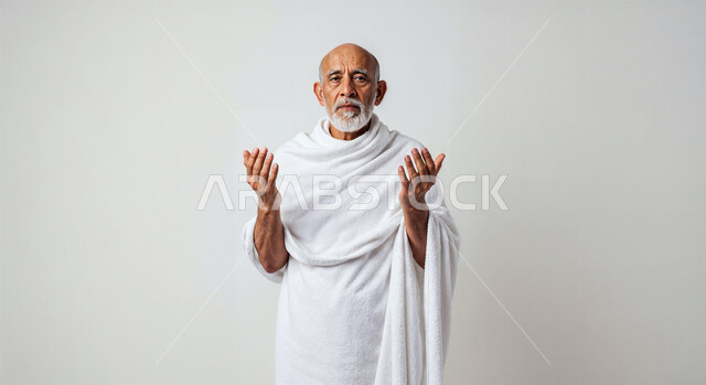 مفهوم أركان الإسلام وأداء الفرائض الدينية، رفع اليدين والدعاء بخشوع وتضرع، بورتريه مقرب لحاج كبير بالسن خليجي عربي سعودي يرتدي ثياب الإحرام يقوم بتأدية مناسك الحج والعمرة، العبادة والتقرب إلى الله، خلفية بيضاء