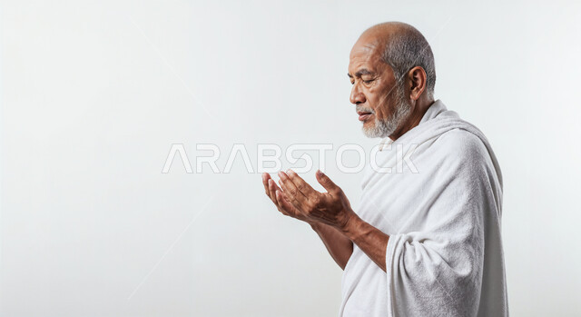 مفهوم أركان الإسلام وأداء الفرائض الدينية، رفع اليدين والدعاء بخشوع وتضرع، بورتريه مقرب من الجانب لحاج كبير بالسن خليجي عربي سعودي يرتدي ثياب الإحرام يقوم بتأدية مناسك الحج والعمرة، العبادة والتقرب إلى الله، خلفية بيضاء