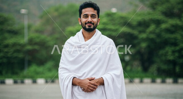 Worship and closeness to God, the concept of the pillars of Islam and performing religious duties, a close-up image of a smiling Saudi Arabian Gulf pilgrim wearing Ihram clothes performing Hajj and Umrah rituals, expressions and gestures of joy and happiness, nature background