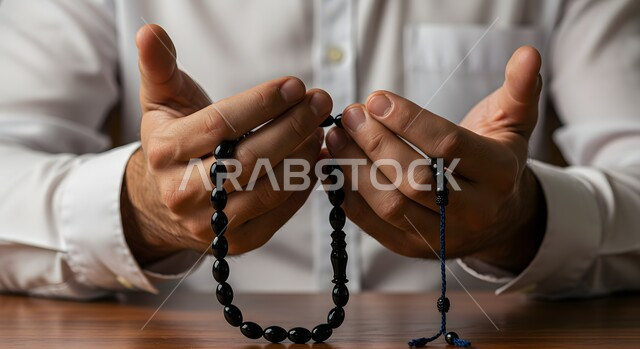  العبادة والطاعة والتقرب الى الله، صورة مقربة ليد رجل عربي خليجي سعودي يرتدي الثوب التقليدي يمسك بيده سبحة من حبات من الخرز السوداء ، التسبيح والتهليل وذكر الله تعالى، الاجتهاد في العبادات