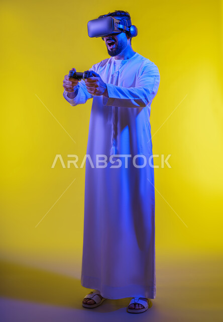 العالم الترفيهى الرقمى ، دمج العالم الخيالي مع المتعة والتسلية، بورتريه لرجل عربي خليجي اماراتي مبتسم يرتدي الكندورة التقليدية ونظارة الواقع الإفتراضي يمسك بيده عصا التحكم يقوم باللعب في ألعاب الفيديو الترفيهية، أجهزة تكنولوجية وتقنيات حديثة، صورة الجسم بالطول الكامل، خلفية صفراء .