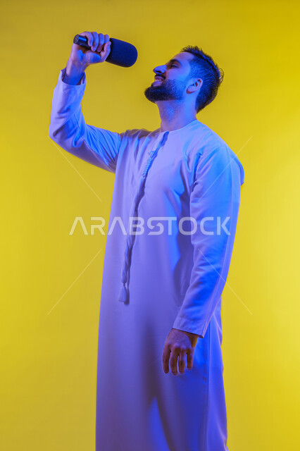 تسجيل مقطع صوتي غنائي، بورتريه لرجل عربي خليجي إماراتي يرتدي الكندورة الإماراتية ويمسك المايكروفون ويغني بحماس، إيماءات الإندماج والتفاعل مع الغناء، تقديم العروض الفنية المسرحية والفقرات الترفيهية، خلفية صفراء .