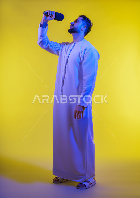 إيماءات الإندماج والتفاعل مع الغناء، تسجيل مقطع صوتي غنائي، بورتريه لرجل عربي خليجي إماراتي يرتدي الكندورة الإماراتية ويمسك المايكروفون ويغني بحماس، تقديم العروض الفنية المسرحية والفقرات الترفيهية، خلفية صفراء .