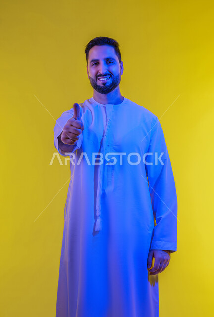 الشعور بالرضا والاستحسان، لامتياز والعلامة الكاملة، التعبير عن الإعجاب والتقدير، رفع اليد بعلامات الجودة والقبول، بورتريه لرجل عربي خليجي اماراتي يرتدي الكندورة ينظر إلى الكاميرا بإيماءات السعادة والسرور، الجسم بالطول الكامل، خلفية صفراء .