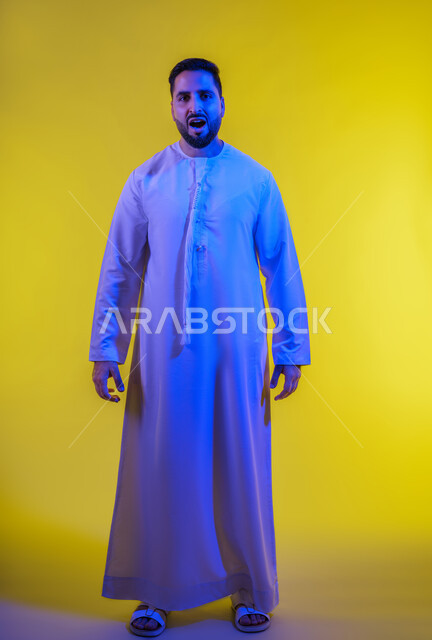 Leaving a safe distance and asking to stop, the concept of disturbance and tension, panic and fear of something, a portrait of an Arab Gulf Emirati man wearing a kandura looking at the camera with gestures of terror and awe, yellow background.