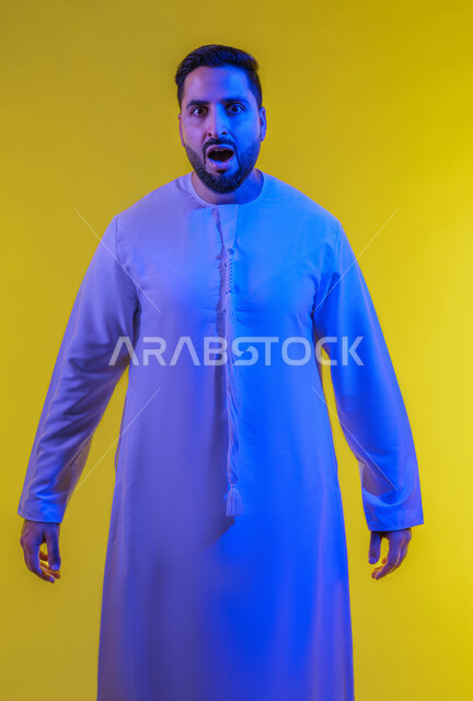الذعر والخوف من شيء ما، مفهوم الاضطراب والتوتر ، بورتريه لرجل عربي خليجي إماراتي يرتدي الكندورة ينظر إلى الكاميرا بإيماءات الرعب والرهبة، ترك مسافة أمان وطلب التوقف، خلفية صفراء .