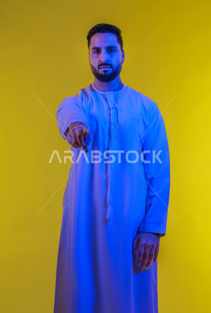 ايماءات التأكد من شيء ما ,التحديد نحو هدف معين, بورتريه لرجل عربي اماراتي خليجي يرتدي الكندورة يشير الى الكاميرا باصبع السبابة , صورة الجسم بالطول الكامل, خلفية صفراء .