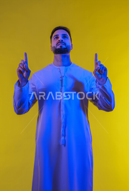 تحديد موقع معين، الدلالة على مكان عنصر، الإشارة و التوضيح إلى شيء ما, بورتريه لرجل عربي خليجي إماراتي يرتدي الكندورة يشير بإصبع السبابة إلى الاعلى ، خلفية صفراء .