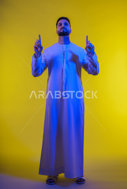 الدلالة على مكان عنصر، الإشارة و التوضيح إلى شيء ما, تحديد موقع معين، بورتريه لرجل عربي خليجي إماراتي يرتدي الكندورة يشير بإصبع السبابة إلى الاعلى ، خلفية صفراء .