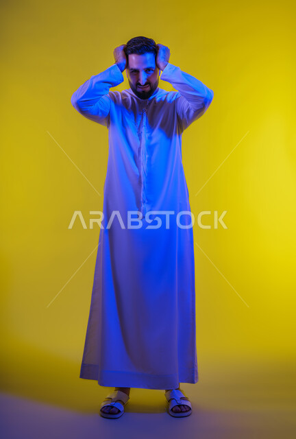 الوقوع في مصيبة, النظر الى الكاميرا بتعابير التعجب, بورتريه لرجل عربي اماراتي خليجي يرتدي الكندورة يضع يديه على رأسه بتعابير الدهشة و الذهول،  المفاجأة و الصدمة عند رؤية شيء ما، الانزعاج عند سماع خبر سيء ، خلفية صفراء .
