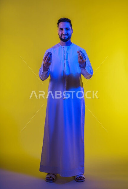 حركة يد وإشارات، الهدوء وطلب الإنتظار، مفهوم الصبر والتريث، إمهال الوقت للقيام بشيء ما،بورتريه لرجل عربي خليجي إماراتي يرتدي الكندورة الإماراتية ويقوم بإيماءات التأن ، صورة الجسم بالطول الكامل ، خلفية صفراء .
