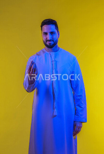 Giving time to do something, being quiet and asking to wait, portrait of an Emirati Gulf Arab man wearing the Emirati kandura and making gestures of patience, deliberation and caution, hand movement and signs, full body image, yellow background.