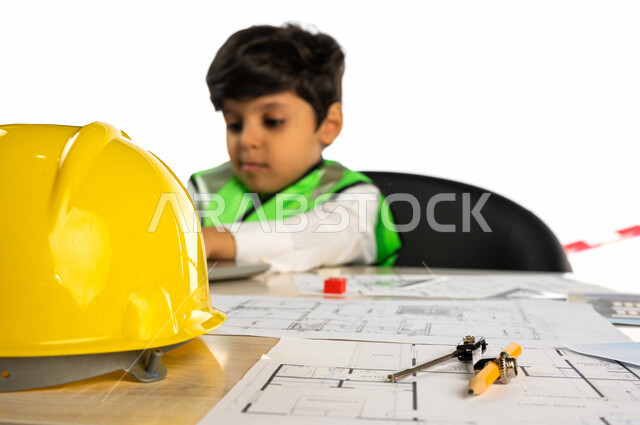 بورتريه لفتى عربي خليجي سعودي داخل مكتب هندسي ، إستخدام جهاز الحاسوب المحمول للبحث ، خوذة الوقاية ، أدوات ومعدات هندسية ، يرتدي سترة الحماية الخاصة بالعمل ، مهنة مستقبلية ، خلفية بيضاء ، مفهوم الهندسة المعمارية ، مهن ووظائف هندسية