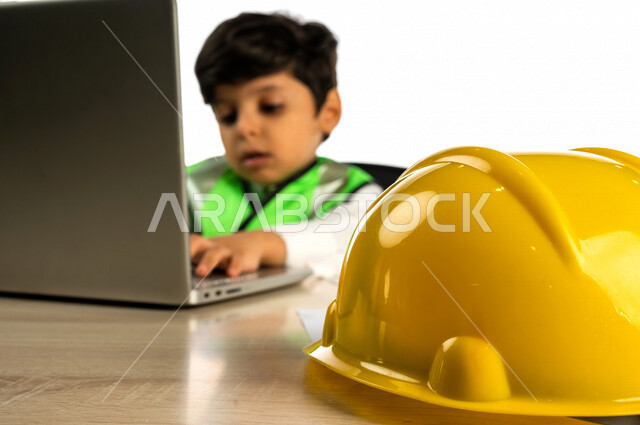 بورتريه لفتى عربي خليجي سعودي داخل مكتب هندسي ، إستخدام جهاز الحاسوب المحمول للبحث ، خوذة الوقاية ، أدوات ومعدات هندسية ، يرتدي سترة الحماية الخاصة بالعمل ، مهنة مستقبلية ، خلفية بيضاء ، مفهوم الهندسة المعمارية ، مهن ووظائف هندسية