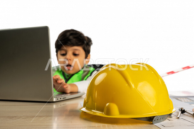 بورتريه لفتى عربي خليجي سعودي داخل مكتب هندسي ، إستخدام جهاز الحاسوب المحمول للبحث ، خوذة الوقاية ، أدوات ومعدات هندسية ، يرتدي سترة الحماية الخاصة بالعمل ، مهنة مستقبلية ، خلفية بيضاء ، مفهوم الهندسة المعمارية ، مهن ووظائف هندسية
