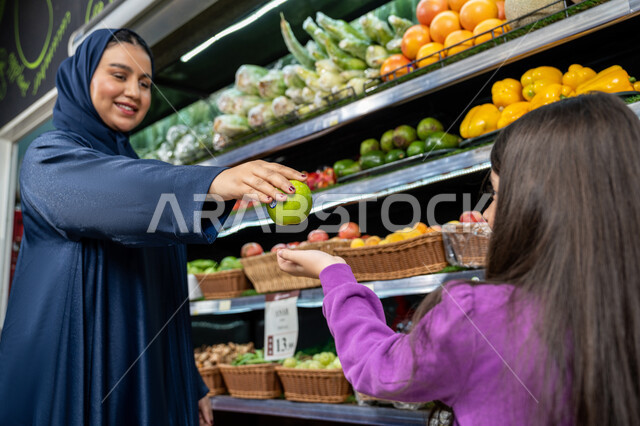 التأثير الإيجابي للتسوق على النساء، ايماءات الفرح والسعاده لقضاء أوقات ممتعه بالتسوق، محاصيل زراعيه وطنية سعوديه، متعة التسوق مع الأبناء، امراة عربية خليجية اماراتية ترتدي العباءة  تقوم بالتبضع من المتجر، ام سعوديه تقوم باعطاء ابنتها ثمره تفاح طازجه