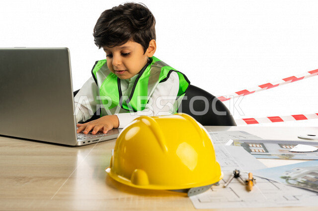 بورتريه لفتى عربي خليجي سعودي داخل مكتب هندسي ، إستخدام جهاز الحاسوب المحمول للبحث ، خوذة الوقاية ، أدوات ومعدات هندسية ، يرتدي سترة الحماية الخاصة بالعمل ، مهنة مستقبلية ، خلفية بيضاء ، مفهوم الهندسة المعمارية ، مهن ووظائف هندسية