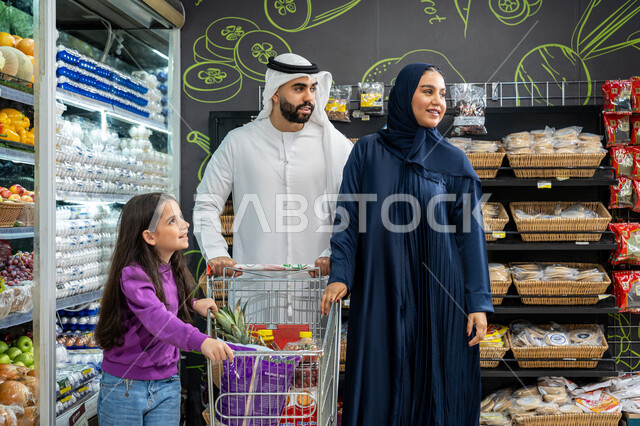 عرض المنتجات والمواد الغذائيه على الارفف في السوبرماركت، الاستفاده من التخفيضات والعروض على المنتجات، أسرة عربيه خليجيه اماراتية مستمتعه بتبضع اللوازم المنزليه من قسم الخضراوات بالسوبرماركت و يقومون بالنظر الي شيء ما، ايماءات الفرح والسعاده لقضاء أوقات ممتعه برفقه العائله