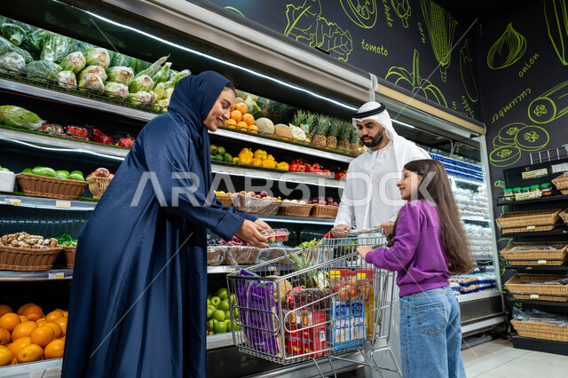 متجر لبيع الاحتياجات والمستلزمات المنزلية، الإستمتاع بالشراء والتبضع بِإيماءات السعاده و السرور، ترابط وتعاون الاسره في التسوق، ام خليجيه تقوم بوضع علبه فراوله في سله التسوق، زوجان عربيان خليجيان اماراتيان يرتديان الزي التقليدي يقومان بالتسوق برفقة ابنتهم، محاصيل زراعيه وطنية اماراتية