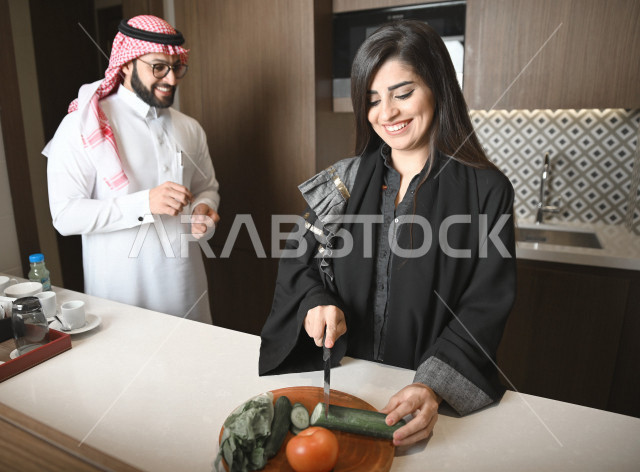 زوجان عربيان خليجيان سعوديان يساعدان بعضهم في اعداد وتجهيز الطعام ، تقطيع الخضراوات لاعداد السلطة الشهية ، تحضير وجبة صحية