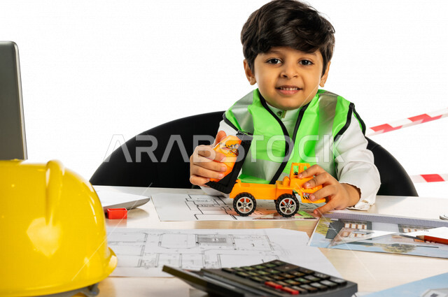 بورتريه لفتى عربي خليجي سعودي داخل مكتب هندسي، بيده لعبة شاحنة خلاطة أسمنت صغيرة، إستخدام جهاز الحاسوب المحمول، أدوات ومعدات هندسية، يرتدي سترة الحماية الخاصة بالعمل ، مخططات وتصماميم هندسية، مهنة مستقبلية، خلفية بيضاء، مفهوم الهندسة المعمارية