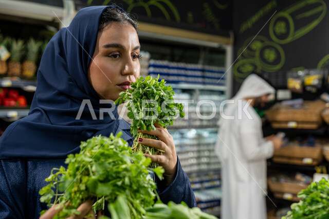 التعاون والتشاور في شراء بعض المستلزمات والحاجات الضرورية، اختيار السلع والمواد الغذائية المختلفة، الاستمتاع بالتسوق في السوبرماركت, زوجان عربيان خليجيان إماراتيان  يقومان بالتبضع ، صورة مقربة لامراءة تقوم باختيار البقدونس الطازج بعناية، محاصيل زراعية وطنيه اماراتية