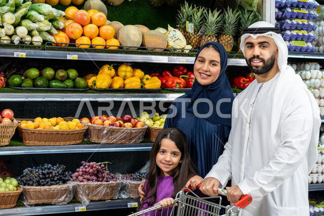 The joy of shopping and buying various goods, cooperation in buying various goods and food items in the supermarket, an Arab Gulf Emirati couple spending enjoyable times shopping and choosing household supplies with their daughter, helping and teaching the children to buy