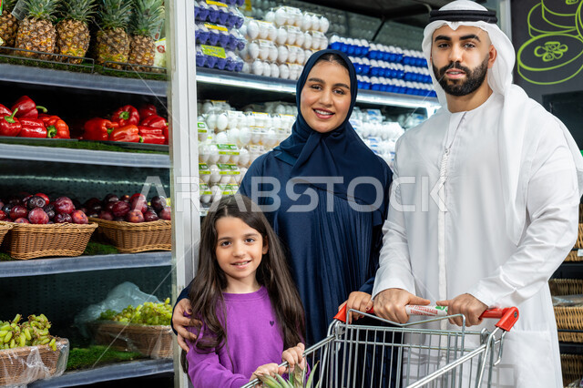 إيماءات السعادة والسرور، التعاون في شراء السلع والمواد الغذائيه المختلفة في السوبرماركت، زوجان عربيان خليجيان اماراتيان يقومان بقضاء أوقات ممتعة بالتسوق واختيار اللوازم المنزليه برفقه ابنتهم، مساعدة وتعليم الأبناء الشراء
