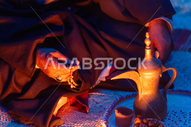 مفهوم الكرم وحسن الاستقبال، ذكرى تأسيس الدولة السعودية الاولى 22 فبراير، يوم بدينا 1727 م، الاحتفال بالمناسبات والأعياد الوطنية، صورة مقربة لرجل عربي خليجي سعودي يرتدي الأزياء التراثية يجلس بجانب دلة القهوة النحاسية، عادات وتقاليد موروثة