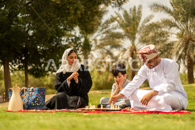 الجلوس في الطبيعة الخضراء، مفهوم التحدي والتركيز، عائلة عربية خليجية عمانية تقضي أوقات ممتعة في إحدى الحدائق في سلطنة عمان، أنشطة عائلية في الأجواء الصيفية، نزهه في الهواء الطلق، التسلية في لعبة الضامة