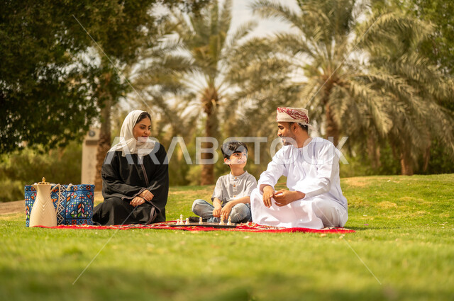 الجلوس في الطبيعة الخضراء، مفهوم التحدي والتركيز، عائلة عربية خليجية عمانية تقضي أوقات ممتعة في إحدى الحدائق في سلطنة عمان، أنشطة عائلية في الأجواء الصيفية، نزهه في الهواء الطلق، التسلية في لعبة الضامة