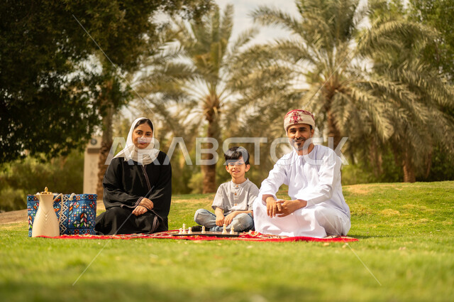 الجلوس في الطبيعة الخضراء، مفهوم التحدي والتركيز، عائلة عربية خليجية عمانية تقضي أوقات ممتعة في إحدى الحدائق في سلطنة عمان، أنشطة عائلية في الأجواء الصيفية، نزهه في الهواء الطلق، التسلية في لعبة الضامة