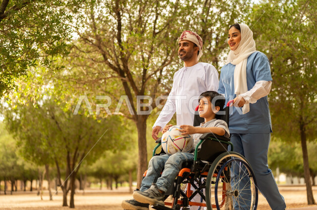 رعاية ذوي الاحتياجات الخاصة، تأمين ادوات تساعد أصحاب الهمم على التنقل، أب يستمتع بالتنزه في إحدى الحدائق في الأجواء الصيفية مع ابنه، الاستعداد للعب بكرة القدم، ممرضة عربية خليجية عمانية محجبة تقوم بمساعدة ولد يجلس على الكرسي المتحرك، نمط الحياة في سلطنة عمان